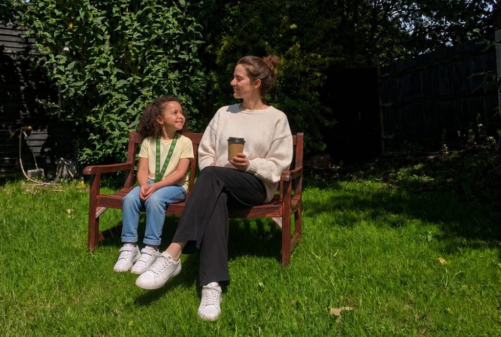 A parent and child chatting on a bench in the garden with coffee