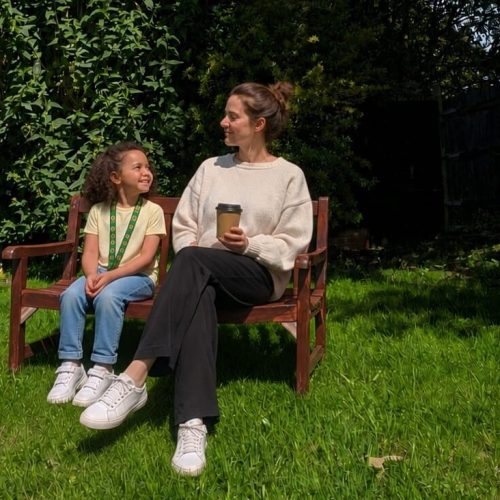A parent and child chatting on a bench in the garden with coffee